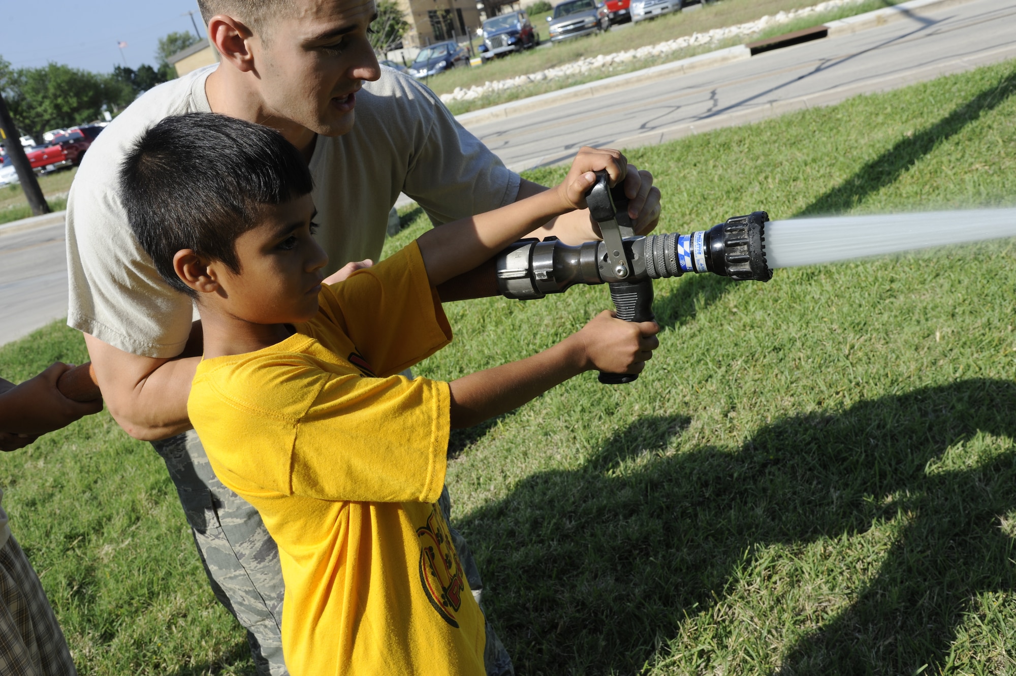 An Airman with the 47th Civil Engineer Squadron helps a student in the Laughlin Education Enrichment Program use a fire hose during a tour of Laughlin Air Force Base, Texas, May 30, 2012. The LEEP program pairs Airmen with underprivileged students in local schools to help the students build self confidence and motivate them to do better in school. (U.S. Air Force photo/Airman 1st Class Nathan Maysonet)