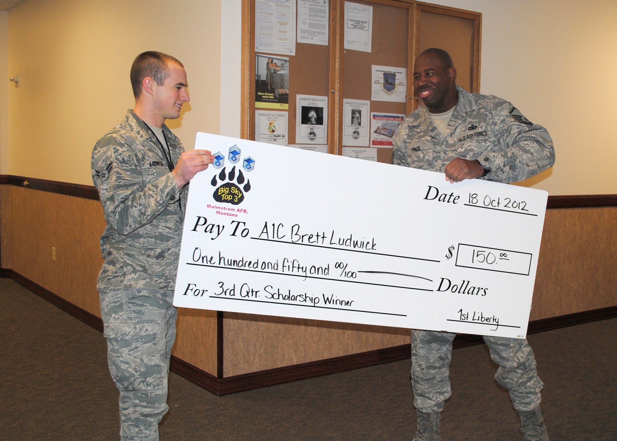 Airman 1st Class Brett Ludwick, 341st Missile Wing command post member, receives a check from Master Sgt. Ronrico Pace, 341st Security Support Squadron logistics and resources flight chief. Luckwick was the recipient of the Big Sky Top 3 Association 3rd quarter scholarship on Oct. 18 after writing an essay on enlisted performance reports. The Top 3 Association offers quarterly scholarships to Airmen grades E1 to E6 that will provide $150 toward tuition or the purchase of books or lab fees. To qualify for the scholarship, an essay is required. It can be no more than three pages in length, double spaced. The 4th quarter scholarship essays’ topic is dress and appearance and is due Dec. 15 to Pace.  (U.S. Air Force photo/Airman 1st Class Katrina Heikkinen)
