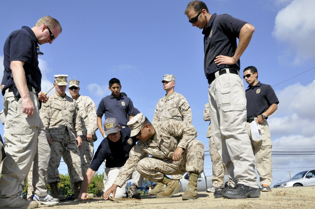 Classmates watch as Jeffery Backus (center), a field training officer here, and Cpl. Anthony Martinez, a patrolman with MP Company, work together to examine footprints during a tracking exercise that is part of a class designed to hone their tracking skills through a new Three-Dimensional Policing Model here Oct. 15-19.