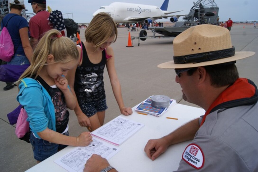 Two girls compare answers on the water safety quiz they are taking at the U.S. Army Corps of Engineers Southwestern Division water safety event at the McConnell Air Force Base Air Show and Open House Sept. 29 & 30. Tulsa District USACE Park Ranger BJ Parkey helps out if the girls get stuck on an answer. Parkey also uses the time to educate them about water safety. When they are done, the girls will earn a water safety giveaway.
