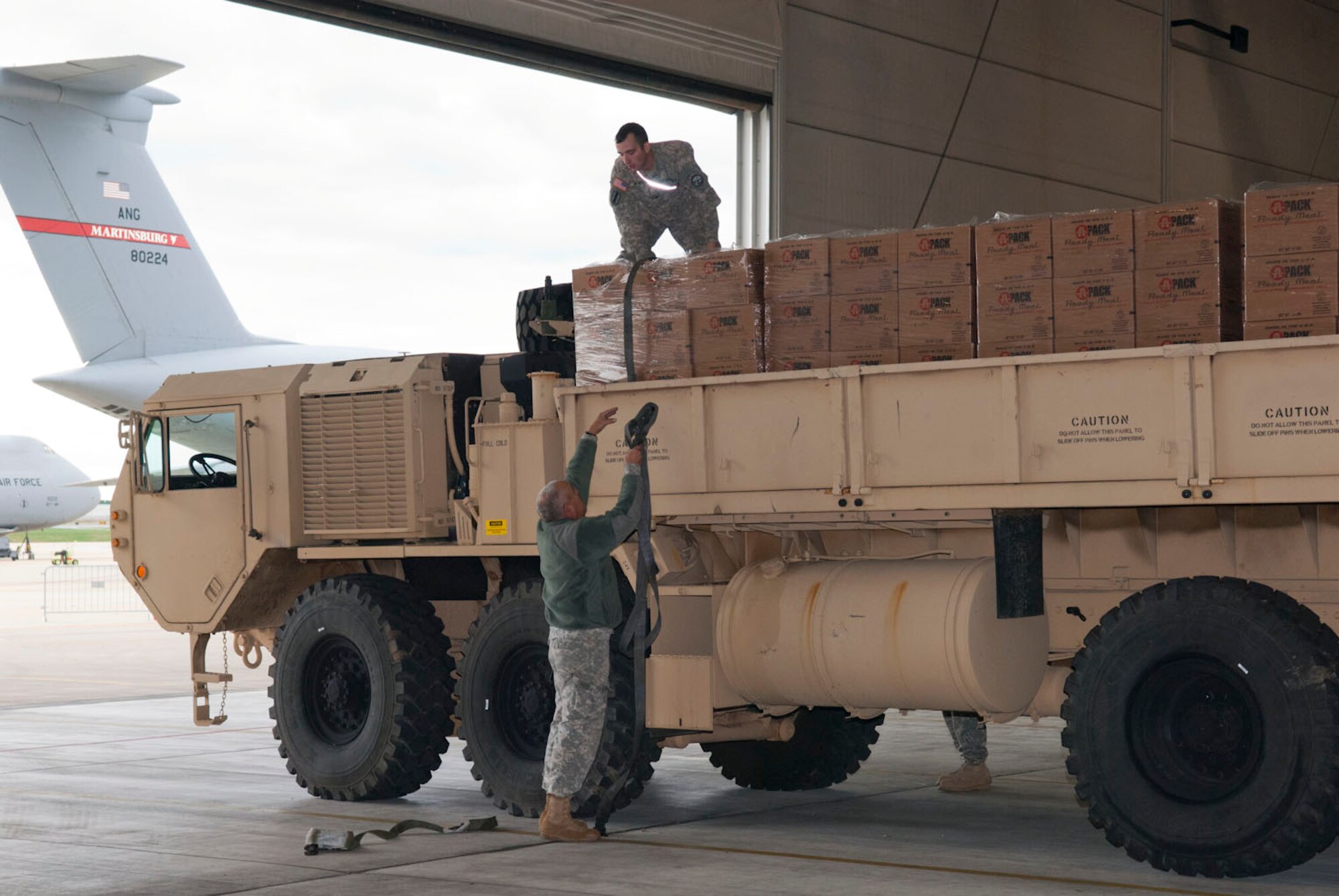 Staff Sgt. Randolph Cutlip hands a strap up to Spc. Craig Brown in a hangar at the 167th Airlift Wing, Martinsburg, W.Va., Nov.2, 2012. The West Virginia National Guardsmen, both assigned to the 77th Brigade’s  201st  Forward Support Company, were assisting with storm relief efforts by transporting pallets of water and boxed meals to counties in West Virginia hit hardest by the storm. The 167th AW is serving as a staging area for disaster relief supplies which will then be transported throughout West Virginia as needed. The West Virginia National Guard has over 200 members aiding in recovery efforts from Hurricane Sandy.  The storm blanketed the state with heavy snow and rains and also had severe winds that left homes and properties damaged.  Guardsmen are involved in numerous aspects of the operations from search and rescue missions to debris removal. (Air National Guard photo by Master Sgt. Emily Beightol-Deyerle)