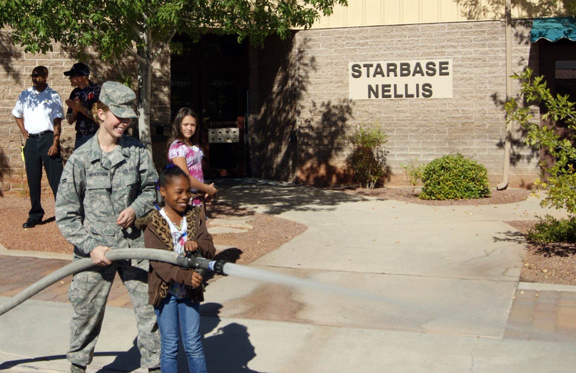NELLIS AIR FORCE BASE, Nev. -- (Front left) Airman First Class Marissa Henderson, 99th Civil Engineer Squadron Fire Protection Flight, shows a student from Lowman Elementary School how to spray a fire here hose Nov. 5. The exhibition was part of a graduation ceremony for the STARBASE Nellis class. STARBASE is a science, technology, engineering and math-focused program geared toward fifth grade students in the Las Vegas Valley. At the completion of the five-day instruction, Airmen from the base demonstrate their job skills to orient the students with different career options. (U.S. Air Force photo/Myles Judd)