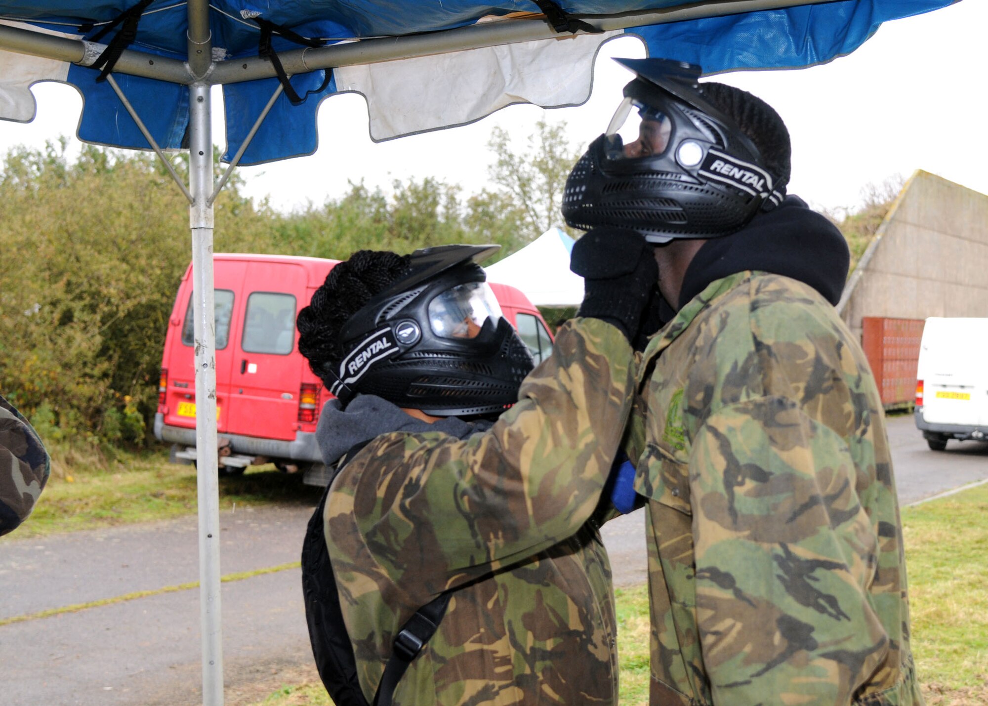 Senior Airman Shakina Shields, 95th Reconnaissance Squadron aviation resource manager, helps Senior Airman Tashee King, 100th Maintenance Squadron metals technician, adjust his face shield at the Single Airman Retreat Paintball Tournament Nov. 3, 2012, on RAF Molesworth, England. The service members were split into three teams by their bases and played on two different courses. The day ended in an all-out free for all. (U.S. Air Force photo by Airman 1st Class Kelsey Waters/Released)