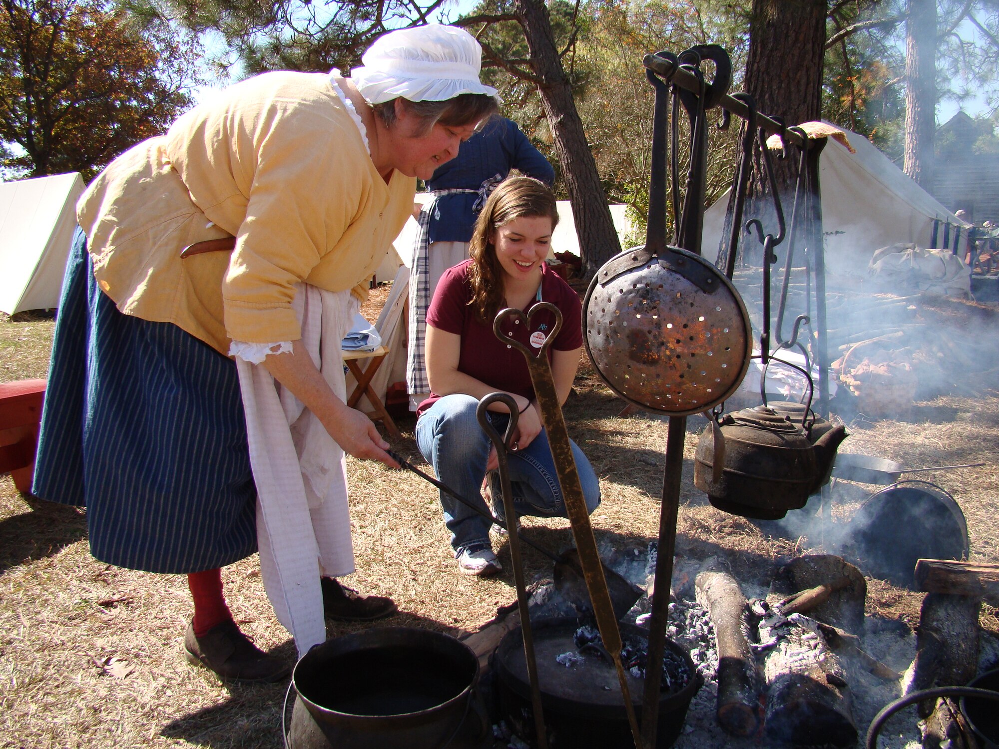 Airman Jodi Lange, 20th Medical Group pharmacy technician,(kneeling) listens as Carol Sherwood, re-enactor, explains Revolutionary War-era cooking methods, at Camden, S.C., Nov. 3, 2012. Lange was a spectator at the reenactment of the Battle of Camden. More than 200 re-enactors, including many military veterans, brought the battlefield back to life 232 years after the event. (U.S. Air Force photo by Rob Sexton/Released)