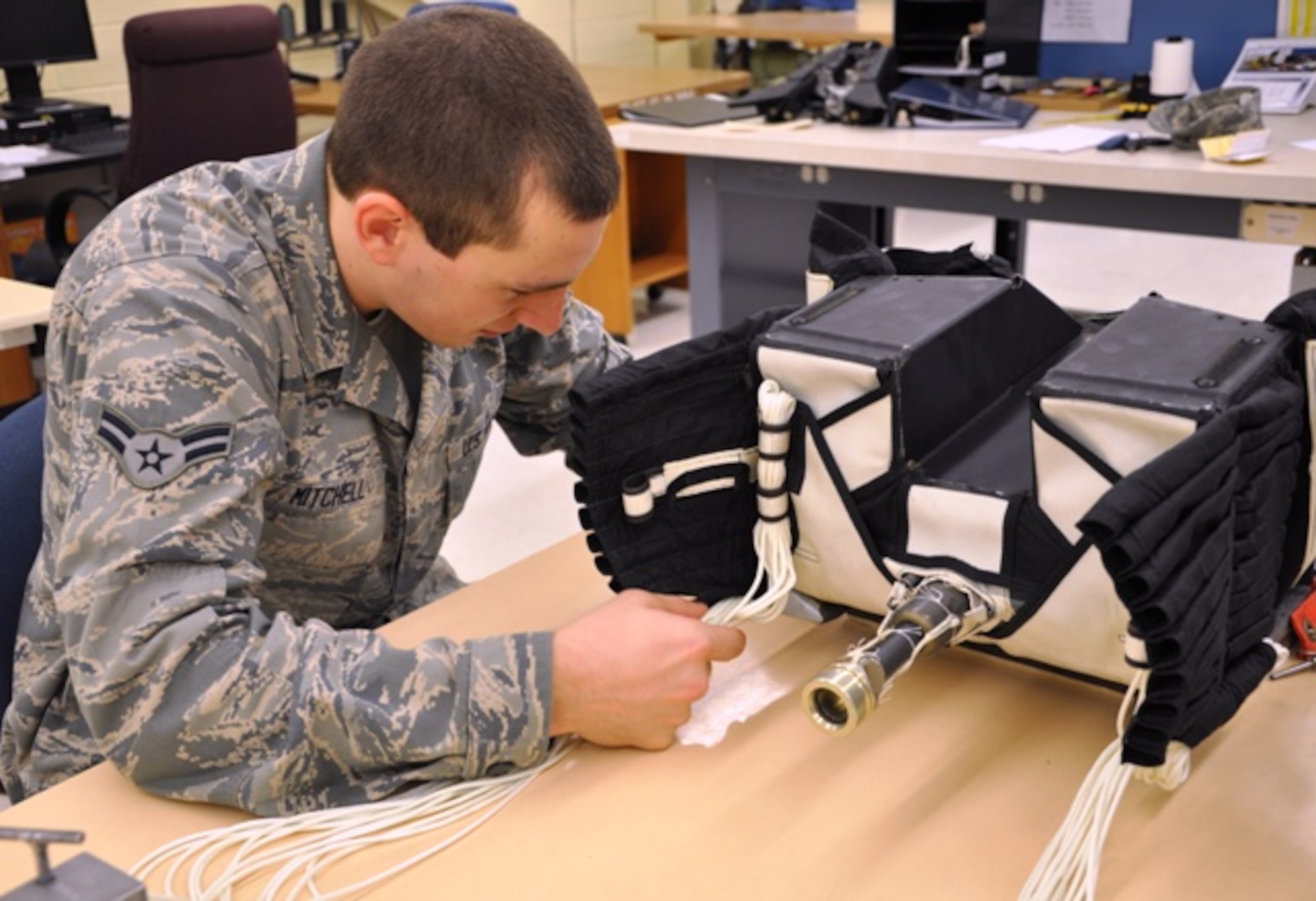 Airman 1st Class Tomas Mitchell, 325th Operations Support Squadron aircrew flight equipment specialist, begins packing the parachute lines into tiny tube-shaped spaces on the outside of the ejection seat container, housing the canopy. The lines have to be carefully threaded through each tube, maintaining an even length. (U.S. Air Force photo by Staff Sgt. Kirsten Wicker) 