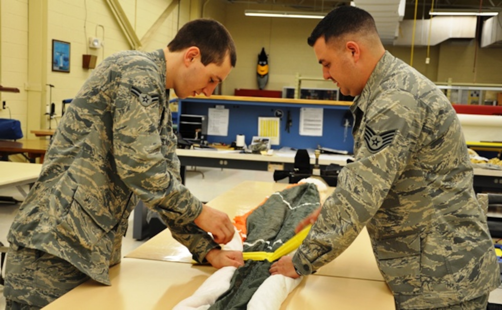 Staff Sgt. Joshua Nelson and Airman 1st Class Tomas Mitchell, 325th Operations Support Squadron aircrew flight equipment specialists, lay small sandbags across the canopy to hold it in place as the material is folded into itself, making it small enough to pack into the ejection seat container. The Airmen must ensure each piece stays even and wrinkle-free throughout the process. (U.S. Air Force photo by Staff Sgt. Kirsten Wicker)  