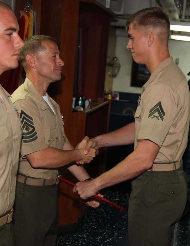 Corporal Marco A. Guillen, logistics combat service support specialist, Combat Logistics Battalion 15, 15th Marine Expeditionary Unit, shakes hands with 1st Sgt. Yomen J. English, 1st Sgt., Weapons Company, Battalion Landing Team 3/5, 15th MEU, during the graduation ceremony for a Corporals course aboard the USS Rushmore, Nov. 2. The Marines devoted 81 hours to physical training, lectures, practical application, performance evaluations, written evaluations and counselings during the course. The 15th MEU is deployed as part of the Peleliu Amphibious Ready Group as a theater reserve and crisis response.