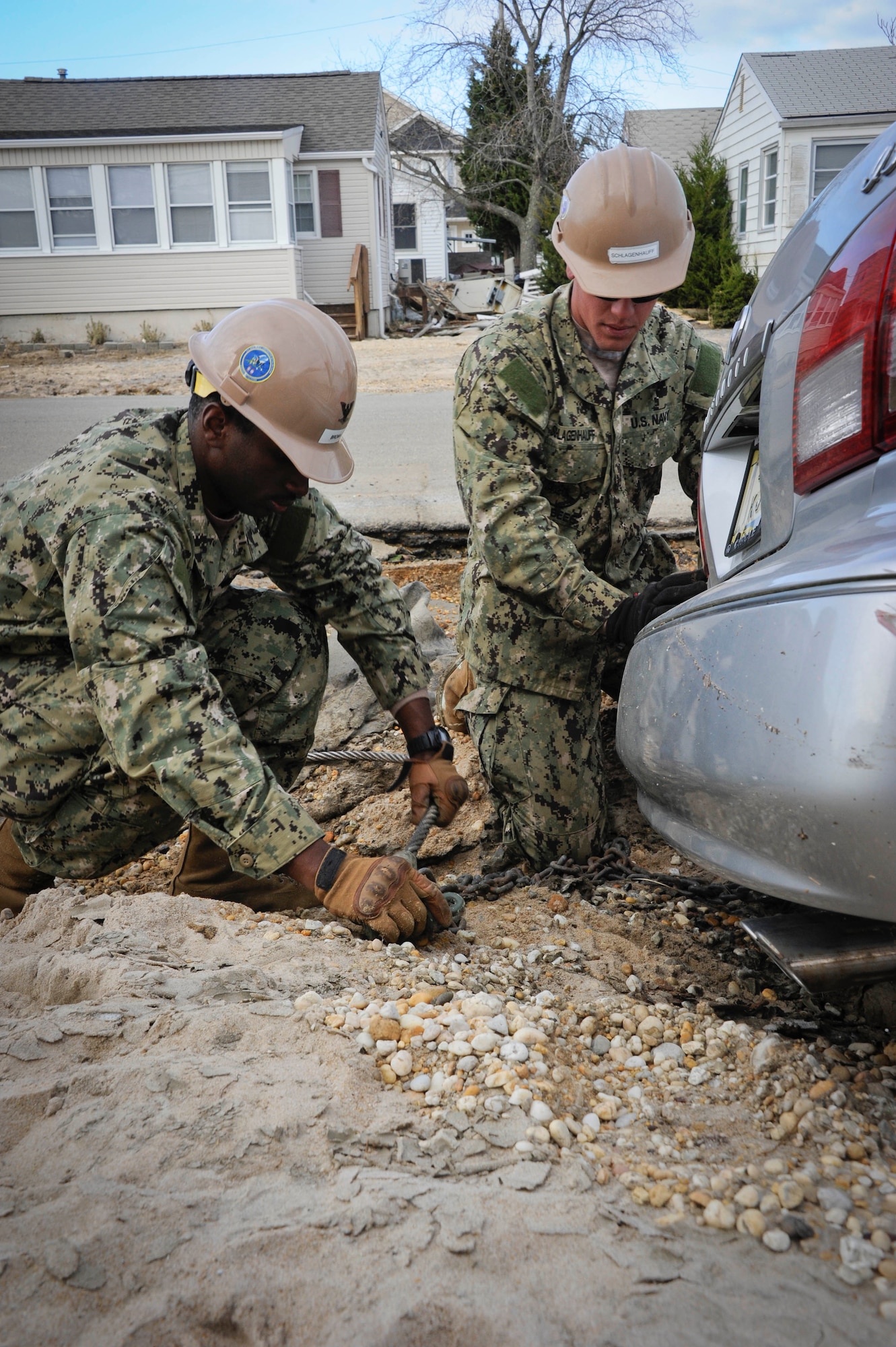 JOINT BASE MCGUIRE-DIX-LAKEHURST, N.J. — (Left) Petty Officer 3rd Class Michael Brown and Seaman Collyn Schlagenhauff, Naval Mobile Construction Battalion 11 construction mechanics, attach chains to a derelict car to be dragged from the sand by a wrecker truck Nov. 6, 2012, Seaside Heights, N.J. NCMB-11 is currently staging out of NCM-21 on JB MDL. The NCMB-11 Sailors, or “Seabees”, are working together to provide relief to the Jersey Coast by way of relocating debris and assessing infrastructure damage. Brown hails from Sierra Vista, Ariz., and Schlagenhauff calls Omaha, Neb., home. (U.S. Air Force photo by Airman 1st Class Ryan Throneberry/Released)