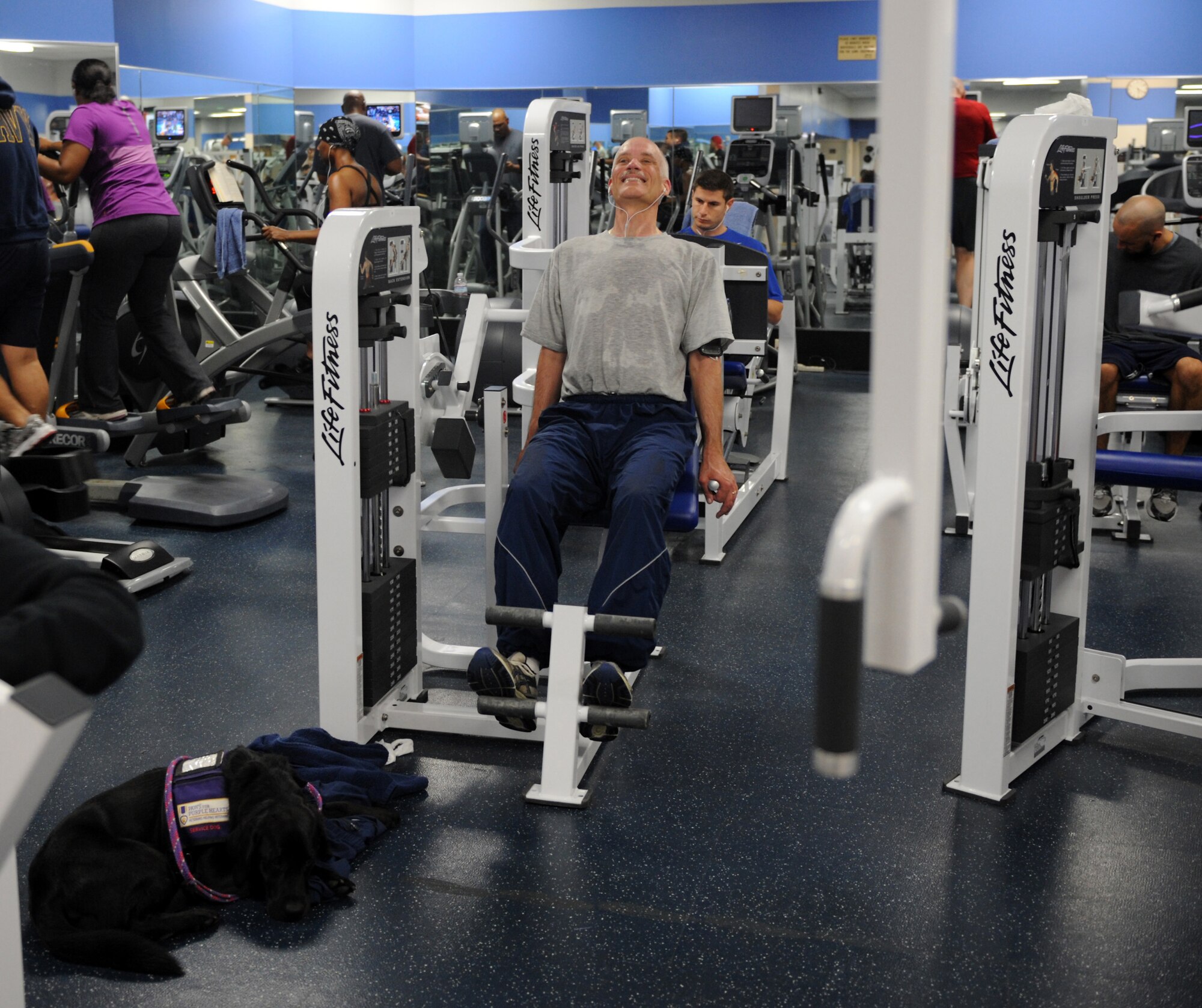 Chief Master Sgt. Richard Simonsen engages in physical activity at the Joint Base Anacostia-Bolling fitness center while his service dog, Yoko, lies next to him. Simonsen lives with Post Traumatic Stress Disorder (PTSD), a condition he endured on a deployment to Afghanistan last year and Yoko helps him with his daily activities. (U.S. Air Force photo/Senior Airman Christina Brownlow)