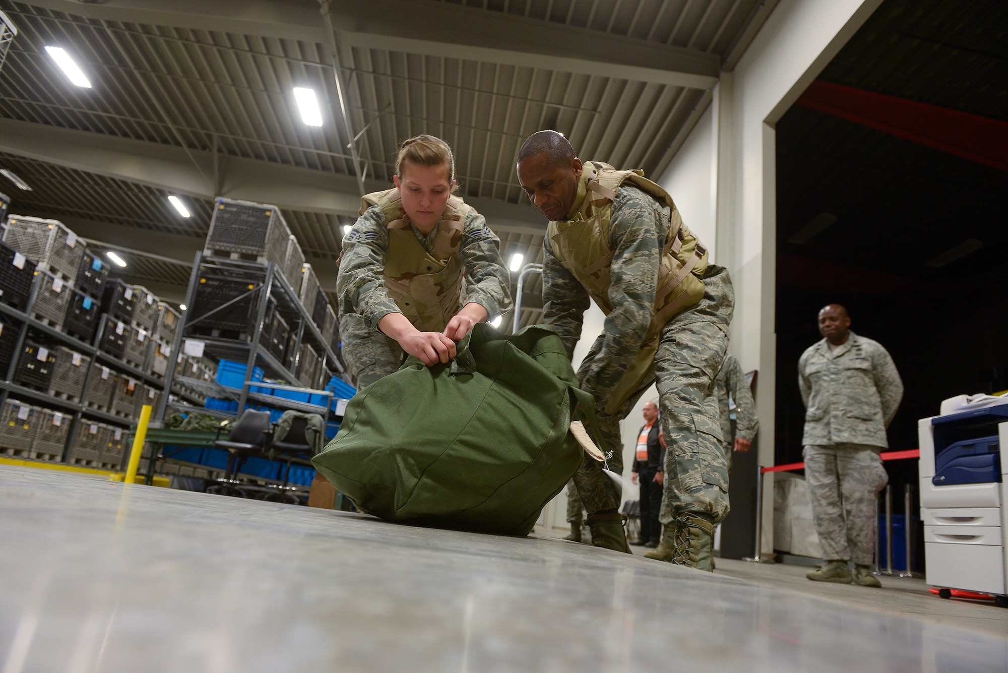 Lt. Gen. Darren McDew, 18th Air Force commander, and Senior Airman Kendra McAlpin, a 19th Logistics Readiness Squadron individual protective equipment journeyman, load a deployment bag onto a pallet here Nov. 6. McDew processed through a deployment line to see what Team Little Rock Airmen are taking with them on deployments. (U.S. Air Force photo by Staff Sgt. Russ Scalf)