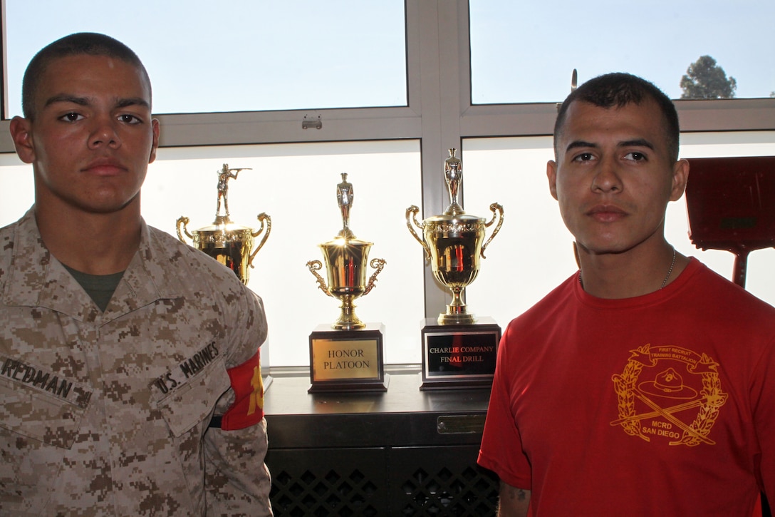 Recruit Troy G. Redman, guide, Platoon 1041, Company C, stands next to Sgt. Juan E. Duque, senior drill instructor, Platoon 1041, Co. C. In the background are trophies their platoon has won such as Honor Platoon. Duque is the drill instructor who selected Redman as guide and has routinely guided Redman on how to be a leader. 