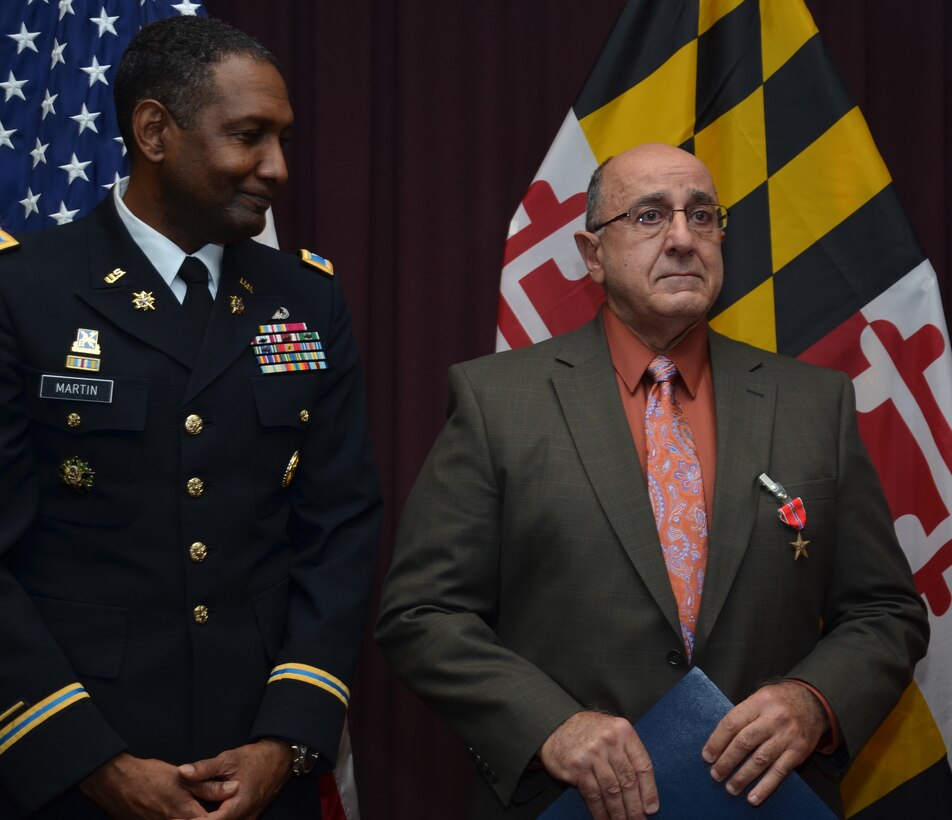 Defense Information School Commandant Army Col. Jeremy Martin, left, looks on after Army veteran and former Spc. 4 Charles Shyab was presented the Bronze Star medal for valor by U.S. Sen. Barbara A. Mikulski during a formal ceremony at DINFOS, Nov. 9, 2012. The ceremony was attended by roughly 250 family members, community leaders, DINFOS staff and students. U.S. Army photo by Spc. Joseph Joynt