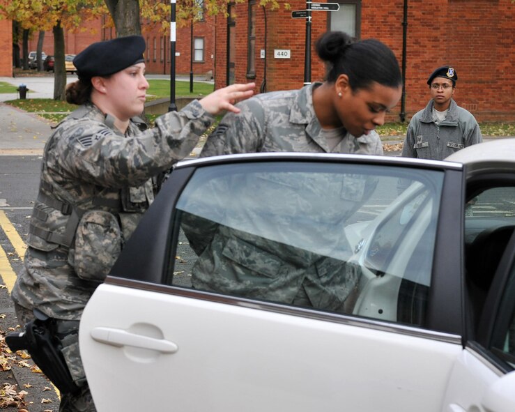 Tech. Sgt. Ashley Tyler, 100th Security Forces Squadron standardization and evaluation team member, watches as security forces patrolman escorts a simulated aggressor into a patrol car Nov. 9, 2012, at RAF Mildenhall, England. As an evaluator, Tyler assesses squadron personnel to ensure job proficiency.(U.S. Air Force photo by Senior Airman Jerilyn Quintanilla/Released)