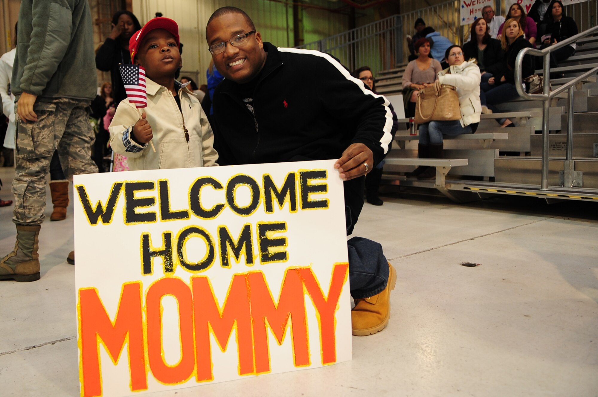 U.S. Air Force Staff Sgt. Thomas McAllister, 4th Aircraft Maintenance Unit, smiles as his son, Kilan McAllister, 3, waves an American flag at a deployment return on Seymour Johnson Air Force Base, N.C., Nov. 14, 2012. The McAllisters awaited the arrival of their wife and mother, Senior Airman Kimberly McAllister, 4th Equipment Maintenance Squadron, from a six-month deployment to the Middle East. (U.S. Air Force photo/Airman 1st Class Aubrey White/Released)