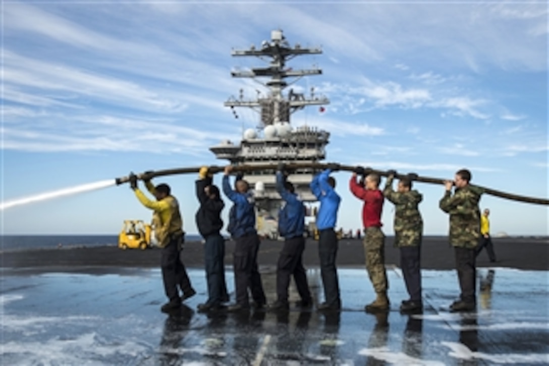 Sailors and Marines hoist a fire hose over their heads as they wash the flight deck of the aircraft carrier USS Nimitz (CVN 68) as the ship operates in the Pacific Ocean on Nov. 12, 2012.  Nimitz is currently in transit to Naval Air Station North Island after successfully completing the ship’s joint task force exercise.  