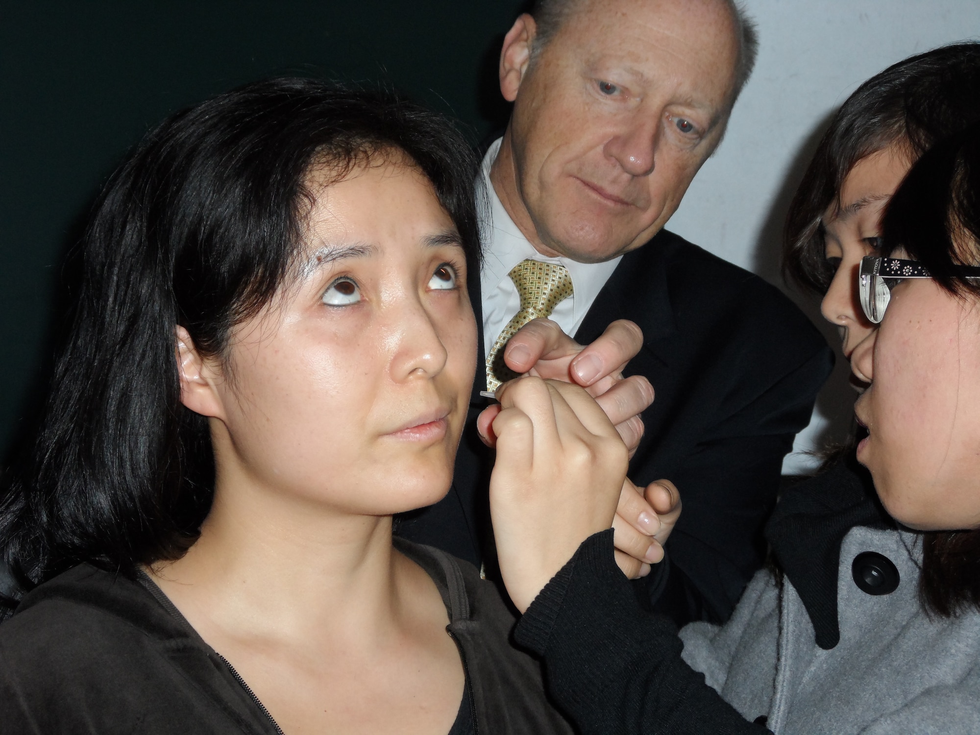 Dr. John Baxter, (middle) Pentagon Clinic Director and acupuncturist, assists a Beijing University of Chinese Medicine student with inserting acupuncture needles into fellow student, Minli Sun's ear Oct. 24, 2012 in Beijing, China. During the medical exchange, Sun explained that she had experience back pain from a car accident that happened when she was 12 years old. She told fellow students her pain was gone after 3 needles of using the battlefield acupuncture procedure. At the invitation of China's People Liberation Army, U.S. Air Force medical physicians, alongside their Chinese military and civilian counterparts, conducted the first-ever Medical Acupuncture Subject Matter Expert Exchange in Beijing Oct. 21-27, 2012. (U.S. Air Force courtesy photo) 
