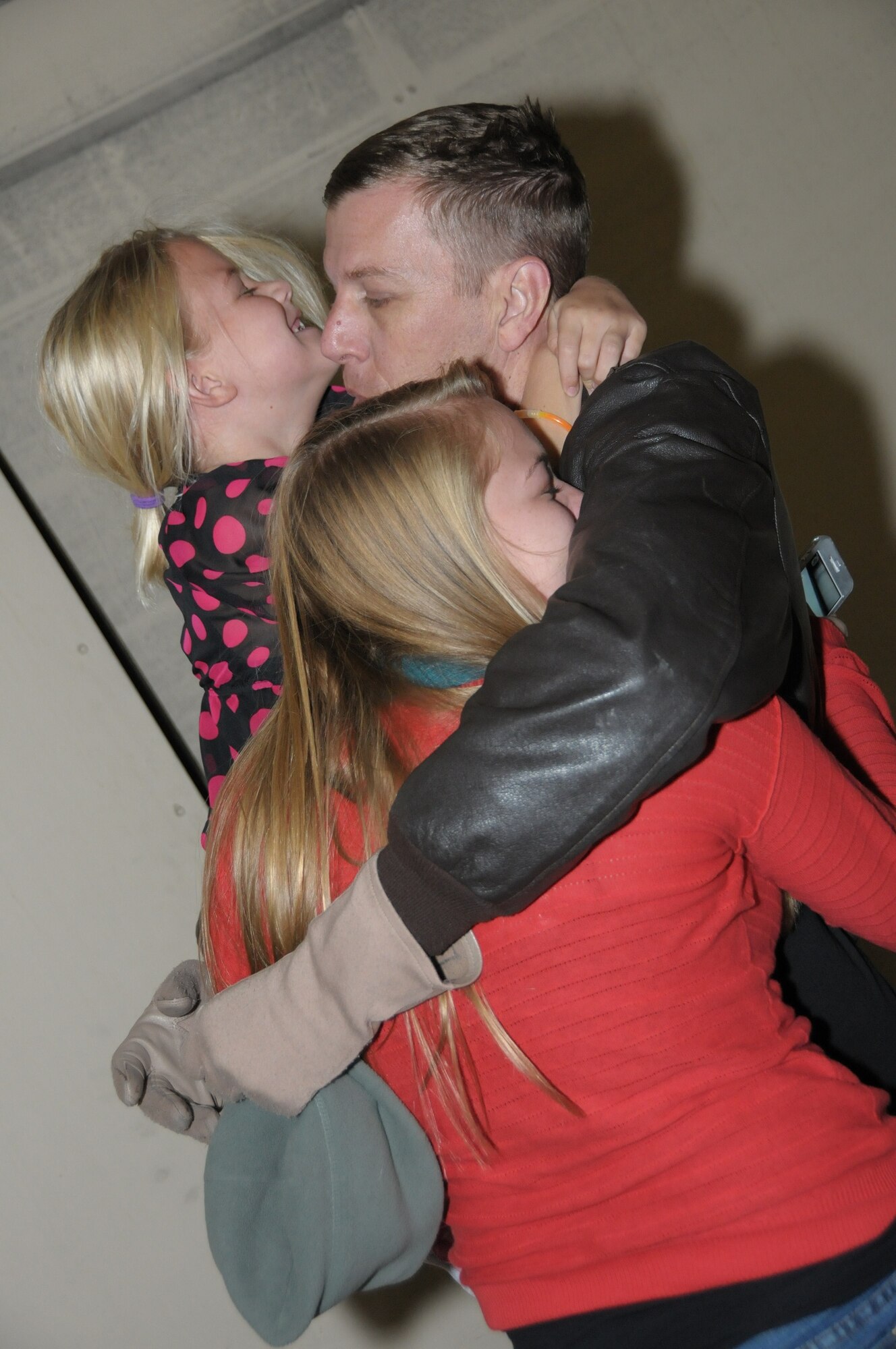 Master Sgt. Elliot Mackay, a Communications Technician assigned to the 970th Airborne Air Control Squadron, hugs his daughters after returning from a six month deployment. (U.S. Air Force Photo by Senior Airman Caleb Wanzer)