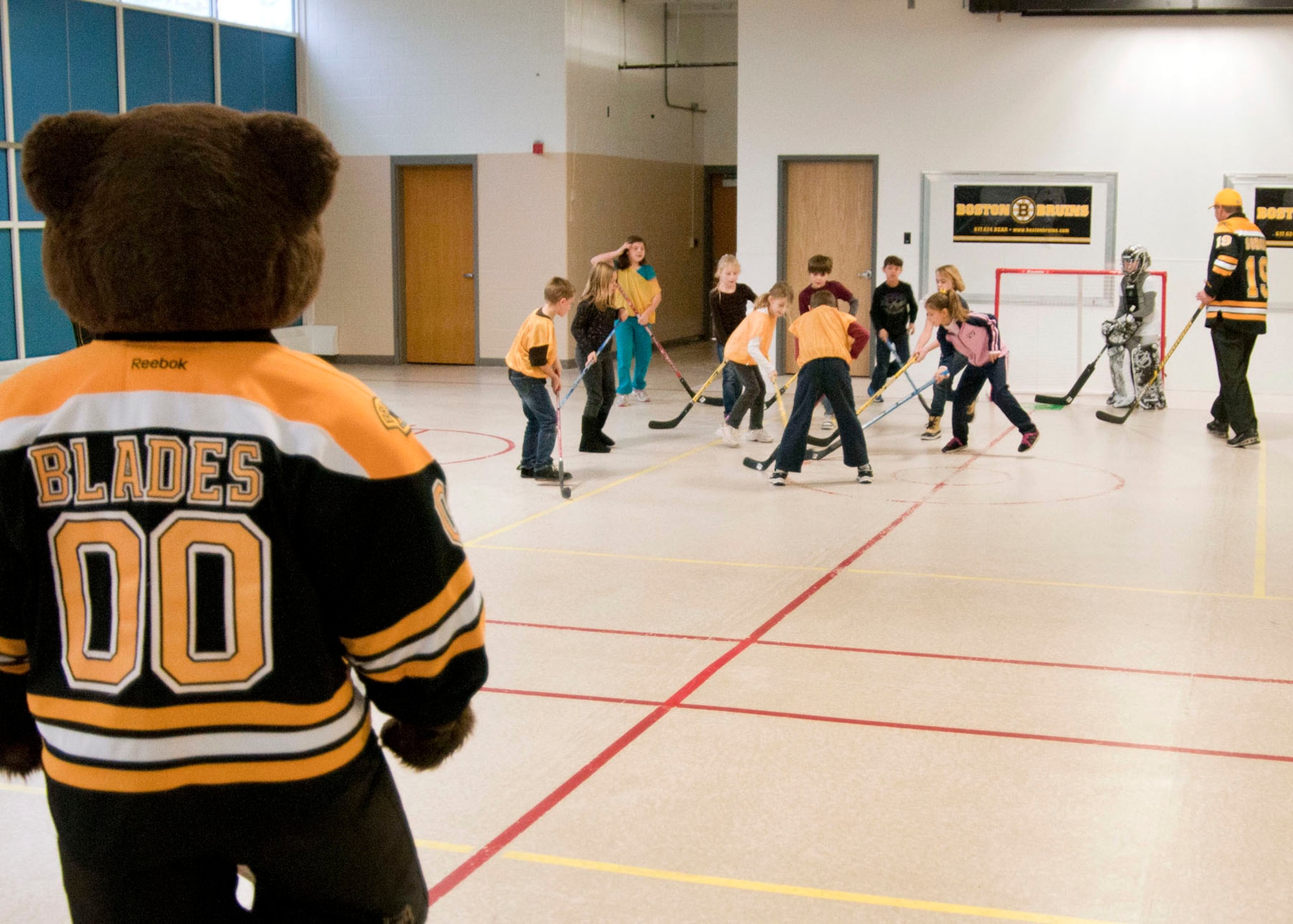 HANSCOM AIR FORCE BASE, Mass. – Boston Bruins mascot, Blades, watches as Bruins alumnus Tommy Songin plays hockey with children at the Hanscom Primary School during a Boston Bruins Youth Development League visit Nov. 8. Bruins staff led children through a number of hockey drills focusing on the fundamentals of play. The team donated the hockey equipment they brought to the school so children could continue to enjoy the game. (U.S. Air Force photo by Mark Wyatt)