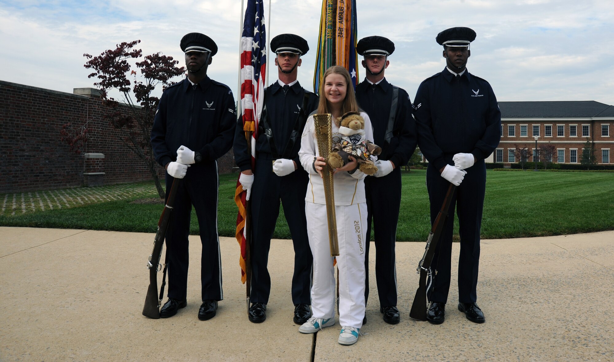 Bailey Reese holds her Olympic torch and Hero the bear as she poses for a personal photo with members of the U.S. Air Force Honor Guard at Joint Base Anacostia-Bolling, D.C., Oct. 24.  Bailey is the president and founder of Hero Hugs, a non-profit organization that sends care packages to service members overseas.  (U.S. Air Force photo/Staff Sgt. Torey Griffith)