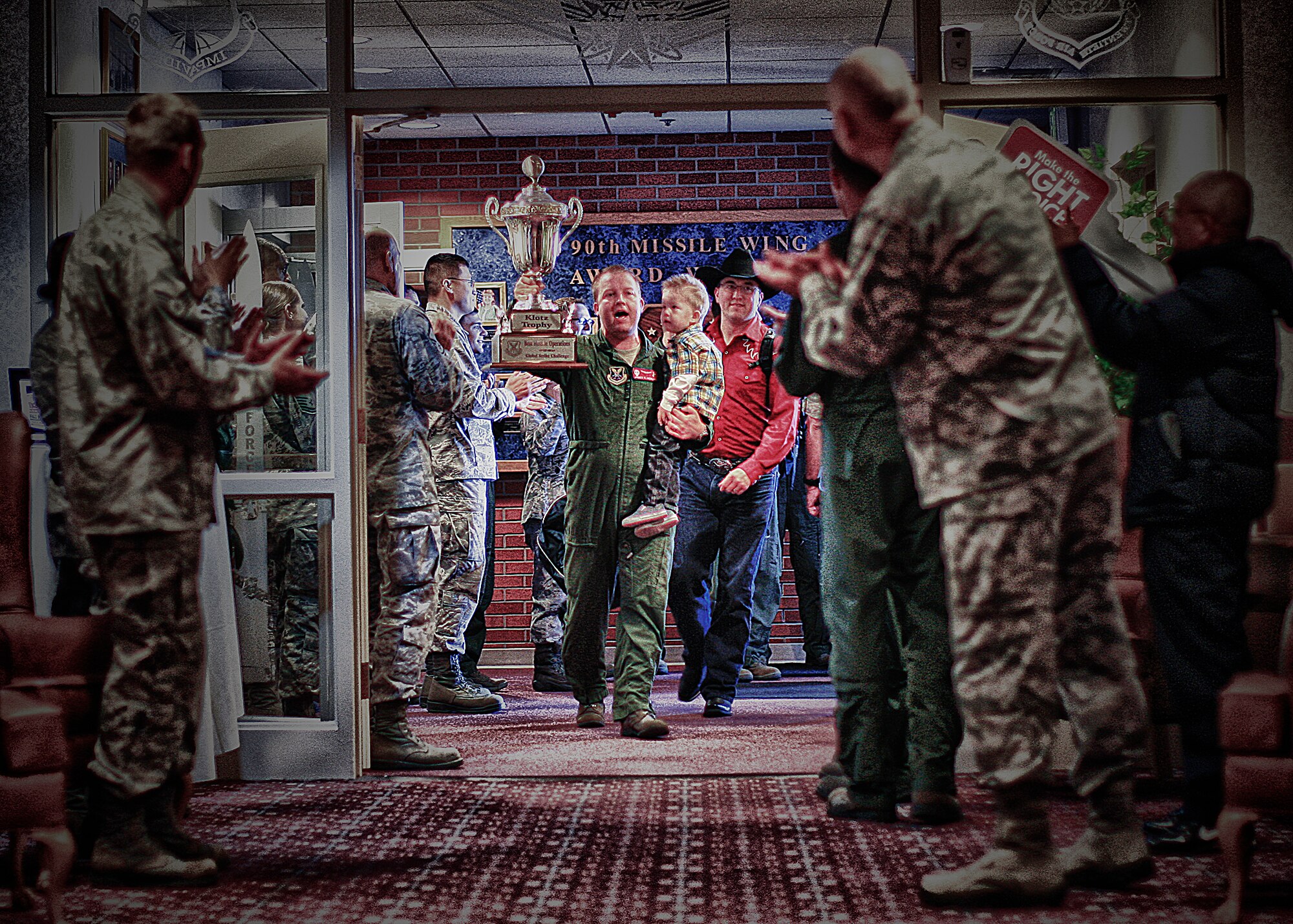 Capt. James Henline, 90th Operations Support Squadron, holds his son in one hand and the Klotz Trophy in the other as he leads the rest of the Warren Wranglers into the Trail's End Club Nov. 8 for a welcome-home celebration. Henline and the Warren Wranglers returned from the Score-posting symposium held at Barksdale Air Force Base, La.
