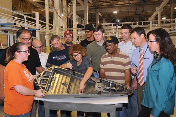 Tinker 76th Propulsion Maintenance Group members huddle around an air frame mounted nozzle sidewall structure, one of four from the F-22 Raptor’s exhaust. Members shown from left are Joanie Miller, sheet metal mechanic; David Oddi, sheet metal mechanic; Jacob O’Connor, AMNS shop supervisor; David Mullens, sheet metal mechanic; Tim Blackwell, water jet operator; Brenda Rawson, sheet metal mechanic; Steven Dorsey, sheet metal mechanic; Bronson Bolvin, water jet engineer; Roy Batts, sheet metal work leader; Justin Sneed, process engineer; Brian Thompson, program manager; and Patricia Welch, maintenance activation process team chief. (Air Force photo by Margo Wright)
