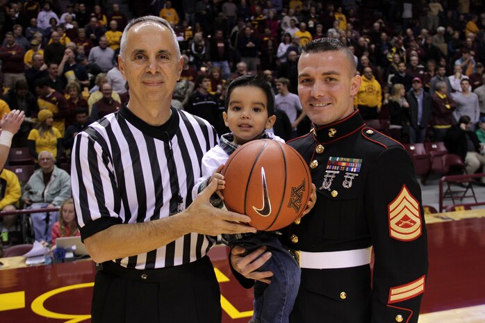 Gunnery Sgt. Roland McGinnis, Officer Selection Station Twin Cities, holds his son, Cristian, after the three-year-old completed his Tip-Off Kid responsibilities at the University of Minnesota men's basketball game at Williams Arena on Nov. 12. For additional imagery from the event, visit www.facebook.com/rstwincities.