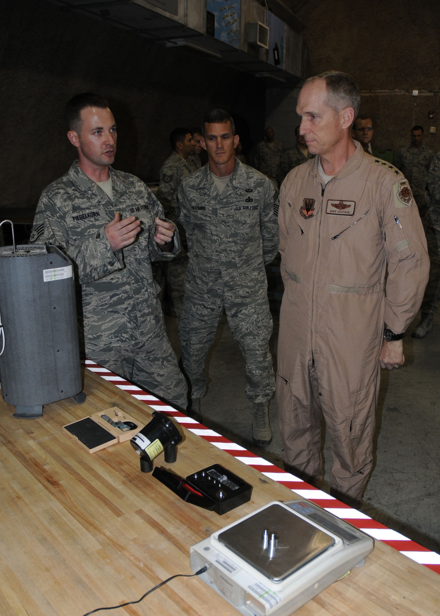 U.S. Air Force Gen. Mike Hostage, commander of Air Combat Command, talks with Staff Sgt. Jordan Fiebelkorn, a Precision Measurement Equipment Laboratory (PMEL) technician, about the various measurement capabilities only available at the 379th Expeditionary Maintenance Group in the U.S. Air Forces Central area of responsibility. Hostage and ACC command chief, Chief Master Sgt. Richard Parsons, toured the Centralized Repair Facility where they were briefed on EMXG capabilities at 379th Air Expeditionary Wing, Southwest Asia.  (U.S. Air Force photo by Capt. Craig Carper/Released)