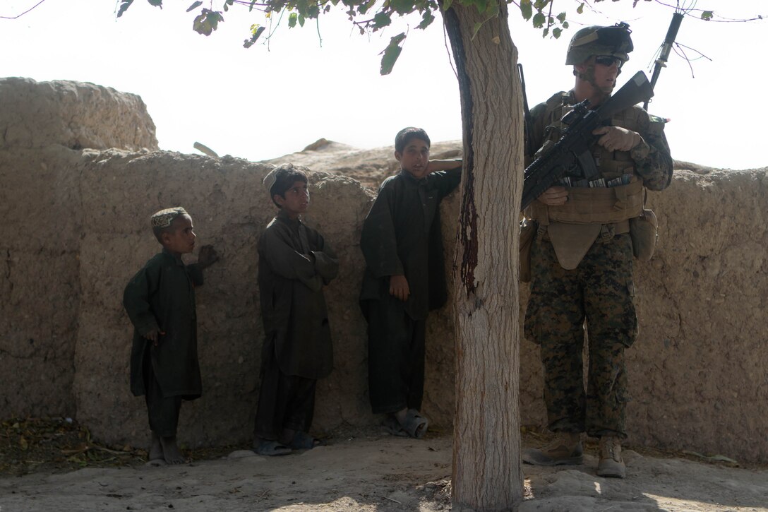 Three curious Afghan boys watch Cpl. Anthony Middleton, team leader, Lima Company, 3rd Battalion, 9th Marines, Regimental Combat Team 7, during a partnered patrol with Afghan National Army soldiers, Nov. 16, 2012. The Marines worked as advisors to the ANA soldiers, teaching them to properly set security and safely sweep through an area.
