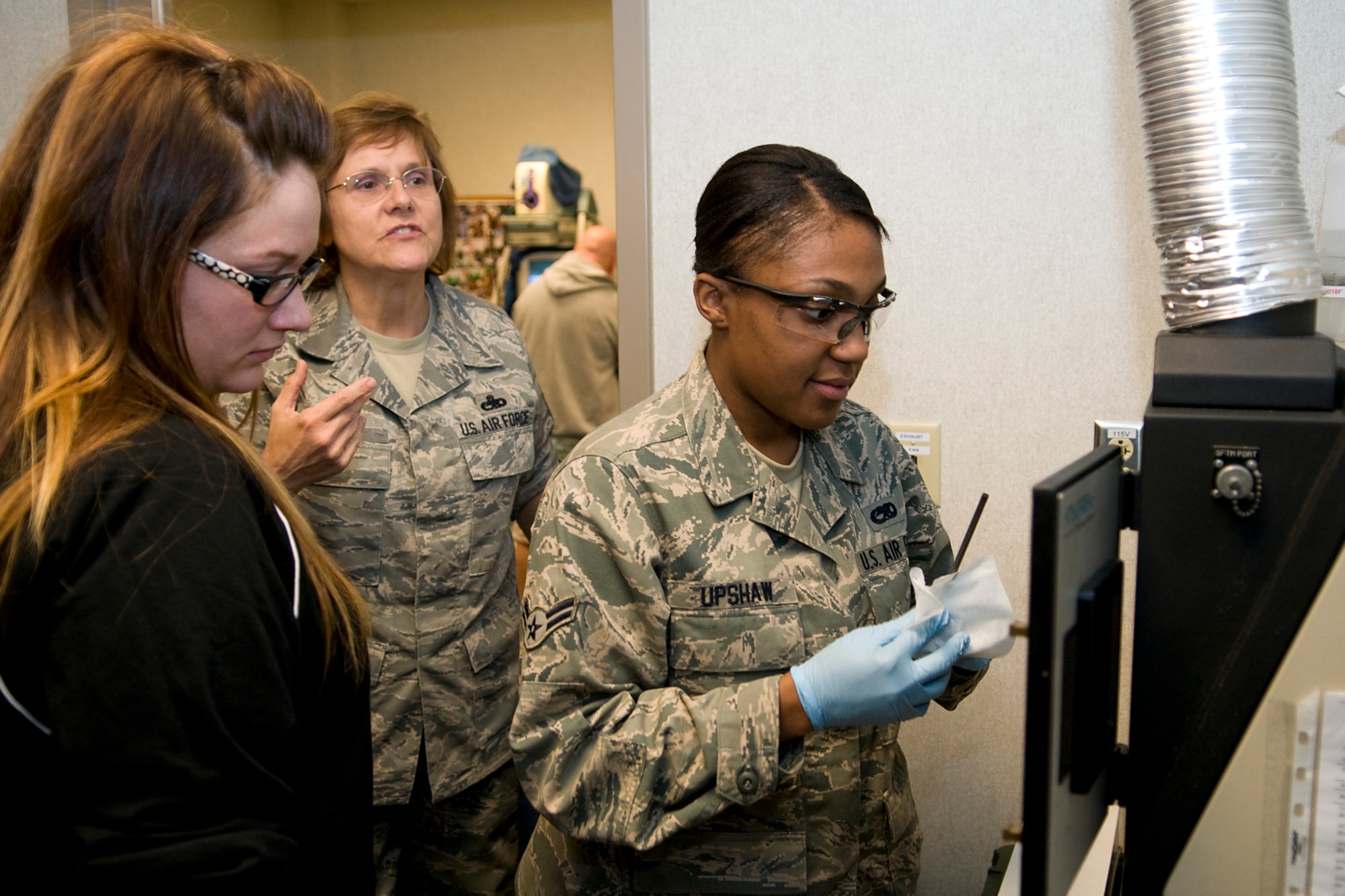 Master Sgt. Valerie Nelson, back, explains to Jessica Green, left, how a spectrometric oil analysis machine burns used engine oil from a KC-135R Stratotanker to determine what might be breaking down inside an aircraft engine as Airman 1st Class Bianca Upshaw, center, demonstrates. Green is the 434th Operations Group honorary commander, Nelson is a 434th Maintenance Squadron nondestructive inspection noncommissioned officer in charge, and Upshaw is a 434th MXS NDI apprentice. (U.S. Air Force photo/ Tech. Sgt. Mark Orders-Woempner)
