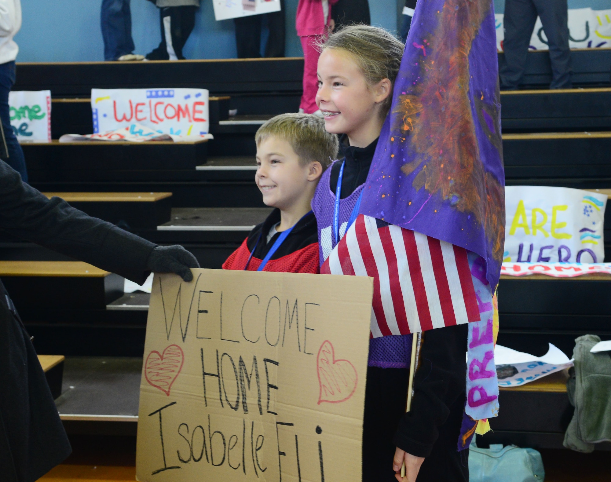 A brother and sister participants for the deployment camp pose for a picture with their welcome home sign and team flag at Aviano Air Base, Italy, Nov. 18. The base hosted a 2-day mock deployment camp for a group of 9 to 15-year-old kids to give them the feel of what their military family members go through during a deployment. More than 40 children participated in several different events from learning how to march to completing an obstacle course.