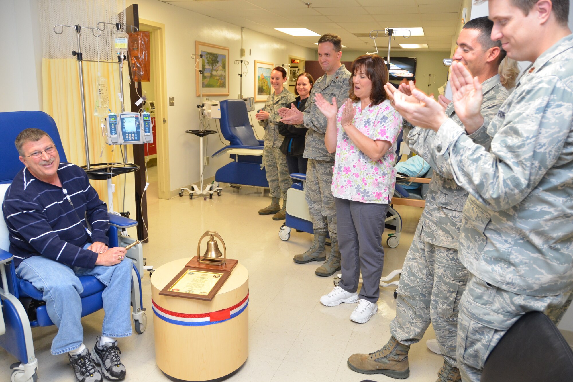 Roger Salois receives a round of applause from members of the hematology/oncology clinic staff and his wife Holly, second from left, after he rang the “Chemotherapy Victory Bell” he had donated to the clinic Nov. 7, 2012 at the 81st Medical Group, Keesler Air Force Base, Miss. From left, staff members are medical technician Airman 1st Class Staci Simpson, Maj. (Dr.) Louis Varner, nurse Jeannie Edge, NCO-in-charge Staff Sgt. Kristopher Iovieno and Maj. (Dr.) Owen Roberts. (U.S. Air Force photo by Steve Pivnick)