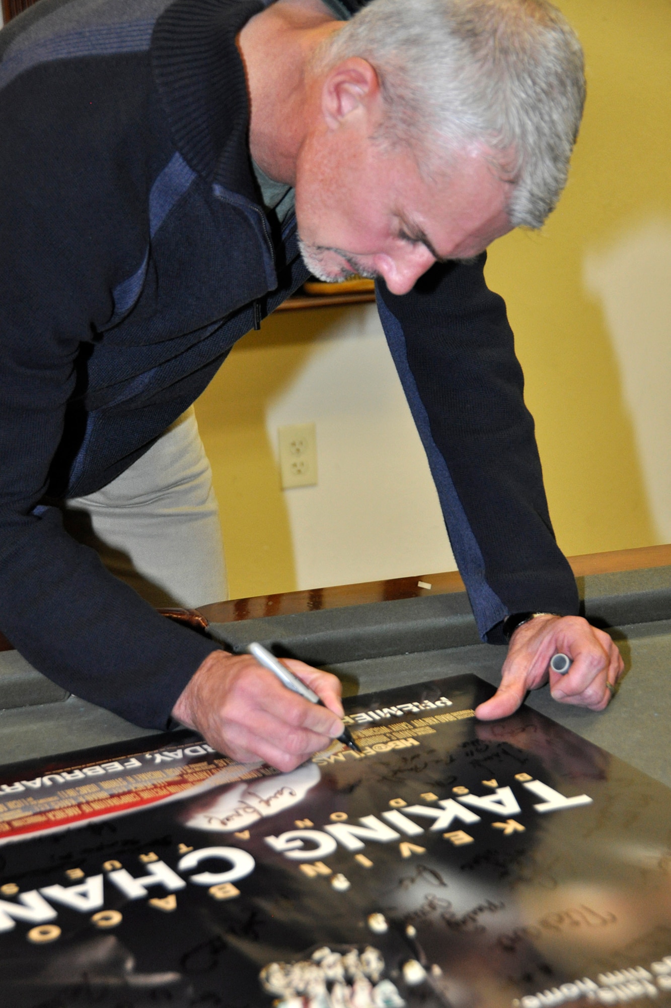 Retired Marine Lt. Col. Michael R. Strobl, signs the "Taking Chance" movie poster in the USO Lounge at the Charles C. Carson Center for Mortuary Affairs Nov. 17, 2012. Strobl's journal of his experience was the basis for the 2009 HBO film. Strobl visited the Port Mortuary in remembrance of his role in escorting Pfc. Chance Phelps remains home for burial. Phelps was killed in action April 9, 2004 while serving in Iraq. (U.S. Air Force photo/Master Sgt. Cherie McNeill)