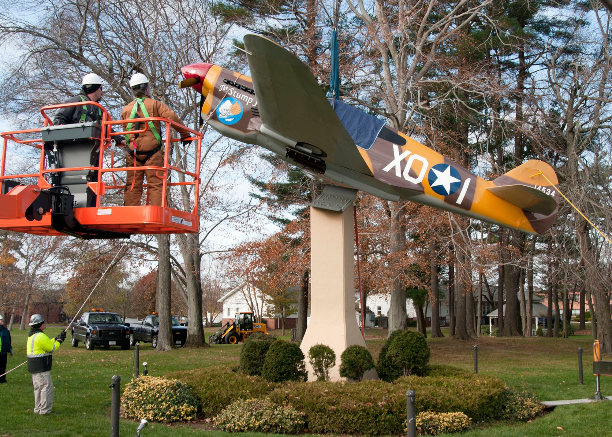HANSCOM AIR FORCE BASE, Mass. -- Workers return the P-40 aircraft to its pedestal on the corner of Vandenberg and Marrett streets Nov. 15 after the completion of a more than three month-long repair and restoration project by base civil engineers. The model received a thorough sanding and several sheet metal panels were replaced before it was primed and painted. (U.S. Air Force photo by Mark Wyatt)