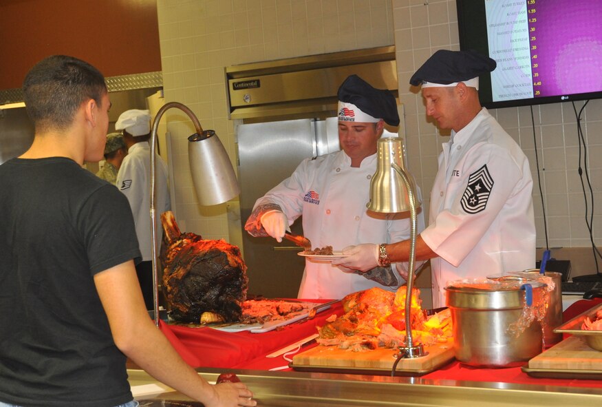 Col. David E. Graff, 325th Fighter Wing commander and Chief Master Sgt. Raymond DeVite, 325th FW command chief, assist the dining facility staff serving a Thanksgiving meal to Airmen in the Berg-Liles Dining Facility Nov. 22 on Tyndall. Each year, the dining facility prepares a Thanksgiving meal for Airmen who may not have a chance to eat a meal somewhere else. (U.S. Air Force photo by 2nd Lt. Andrea
Valencia)
