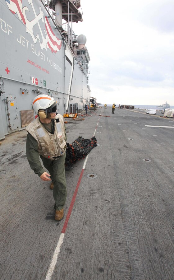 A Marine with the 24th Marine Expeditionary Unit's combat cargo section removes cargo net from the flight deck after a shipment of food and supplies was delivered by an MH-60S Knight Hawk helicopter to USS Iwo Jima during a replenishment at sea detail, or RAS, Nov. 24, 2012. During the RAS the USS Iwo Jima took on fuel, fresh fruits, vegetables, and various supplies to sustain the ship and crew while underway. The 24th Marine Expeditionary Unit is deployed with the Iwo Jima Amphibious Ready Group in the 6th Fleet area of responsibility serving as an expeditionary crisis response force capable of a variety of missions, from full-scale combat to evacuations and humanitarian assistance. Since deploying in March, they have supported a variety of missions in the U.S. Central, Africa and European Commands, assisted the Navy in safeguarding sea lanes, and conducted various bilateral and unilateral training events in several countries in the Middle East and Africa. (U.S. Marine Corps photo by Lance Cpl. Tucker S. Wolf/Released) 