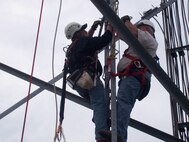Two Safety Specialists from Safety Department demonstrate an aerial rescue during a simulated fall from a communication tower; notice the fall protection harness and related equipment donned by both.