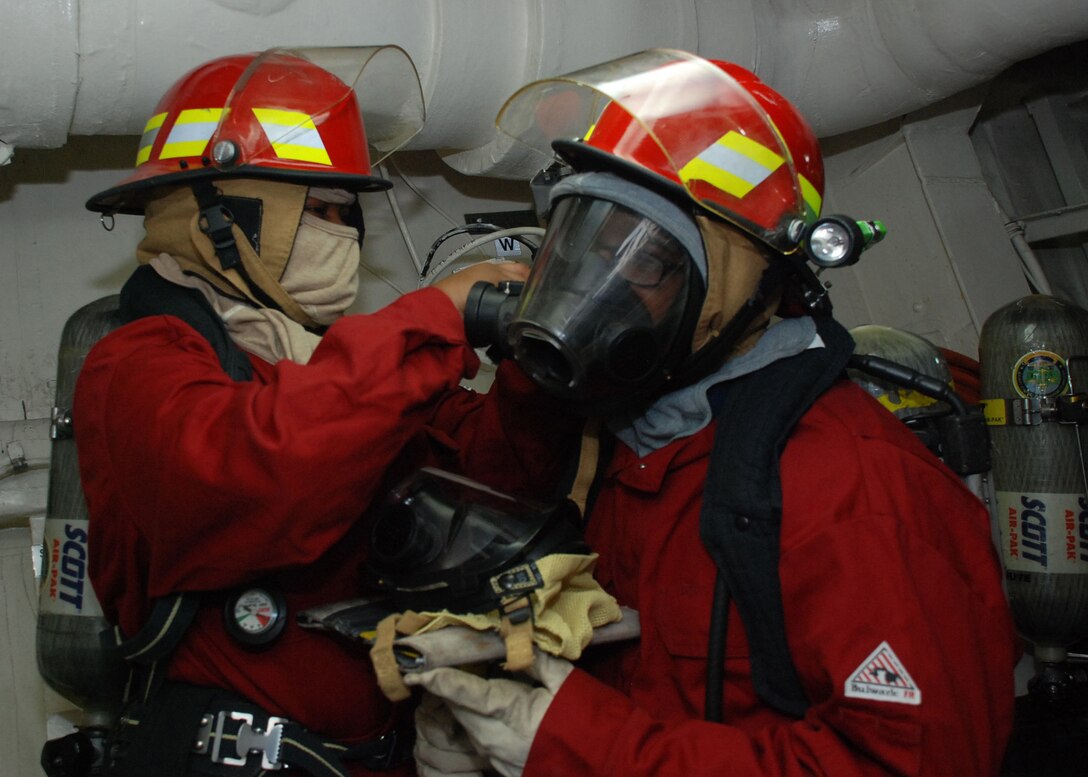 Culinary Specialist 3rd Class Brenai Garner helps a hose team member put on their firefighting equipment during a main space fire drill aboard amphibious transport dock ship USS Green Bay (LPD 20). Green Bay is part of the Peleliu Amphibious Ready Group, with the embarked 15th Marine Expeditionary Unit, and is deployed in support of maritime security operations and theater security cooperation efforts in the U.S. 5th Fleet area of responsibility. (U.S. Navy Photo by Mass Communication Specialist 1st Class (SW/AW) Elizabeth Merriam)