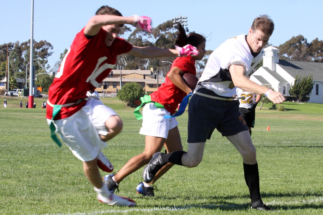 Petty Officer 3rd Class Mathew Petree, a corpsman at 13 Area Branch Medical Clinic, bulldozes Max Jenkins, a server at a Las Vegas restaurant, leaving Hot Route’s halfback, Jade Stevenson, a Las Vegas nanny, exposed during the Buddy Bowl flag-football tournament here Nov. 24. The non-profit event provides service members and the local community a charity based opportunity to interact and compete.