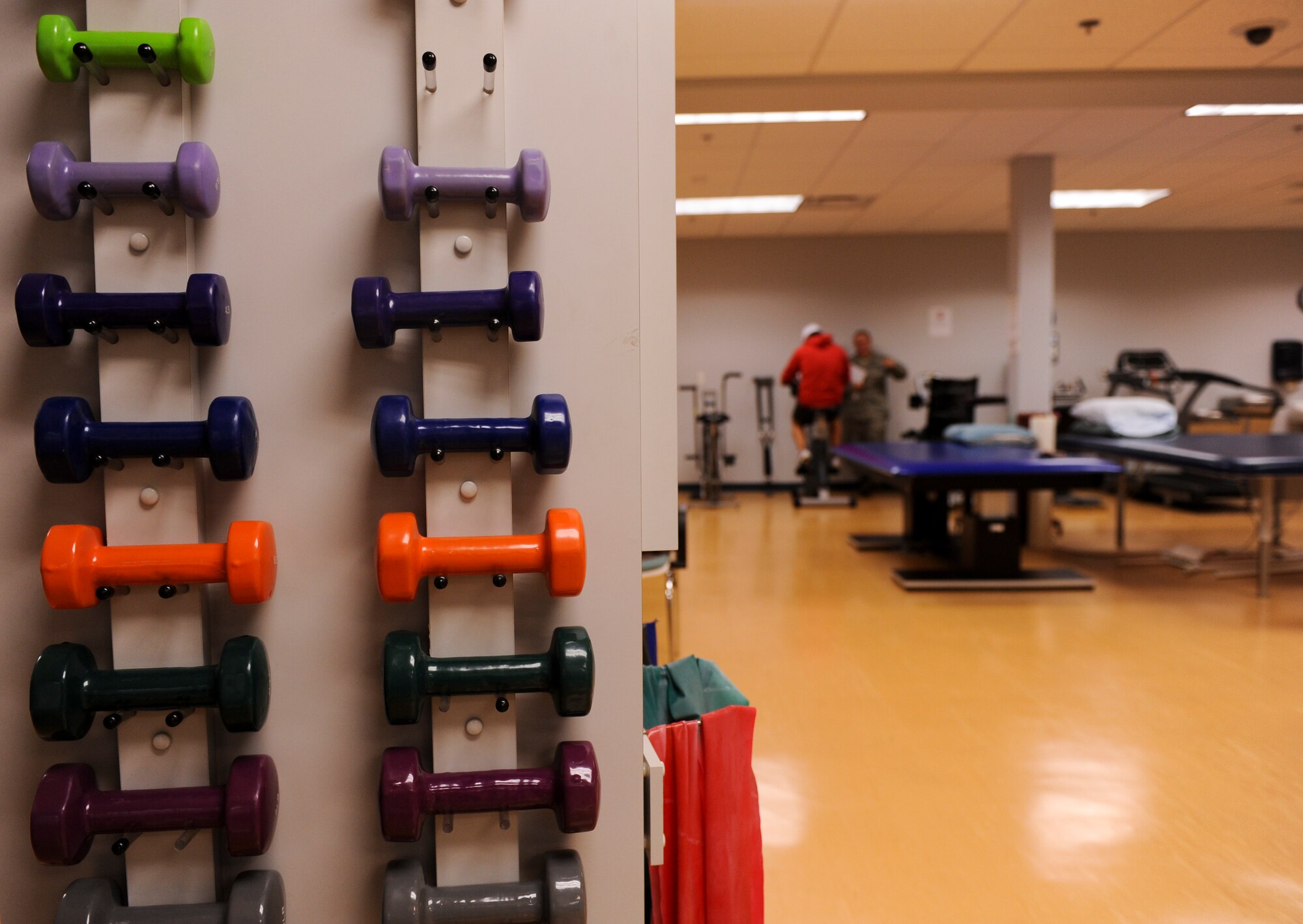 Dumbbells are displayed on a rack as Staff Sgt. David Pienta, a 19th Medical Operations Squadron physical medicine technician, works with a patient on a bike Nov. 7, 2012, at Little Rock Air Force Base, Ark. The 19th MDOS physical therapy staff uses a variety of treatments on patients including strength and conditioning. (U.S. Air Force photo by Airman 1st Class Rusty Frank)