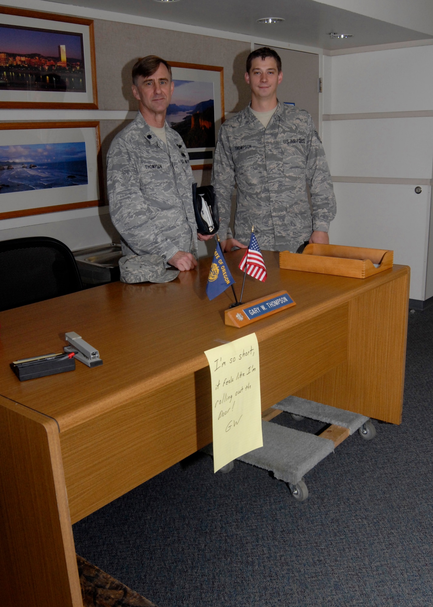 Oregon Air National Guard Lt. Col. Gary W. Thompson and his son Staff Sgt. Joshua Thompson stand behind Gary’s desk as it has been put on weeks in the hallway to open his old office on his last day of active duty service, Oct. 31, 2012 at the Portland Air National Guard Base, Portland, Ore. (U.S. Air Force photo by Tech. Sgt. John Hughel, 142nd Fighter Wing Public Affairs / released)  

