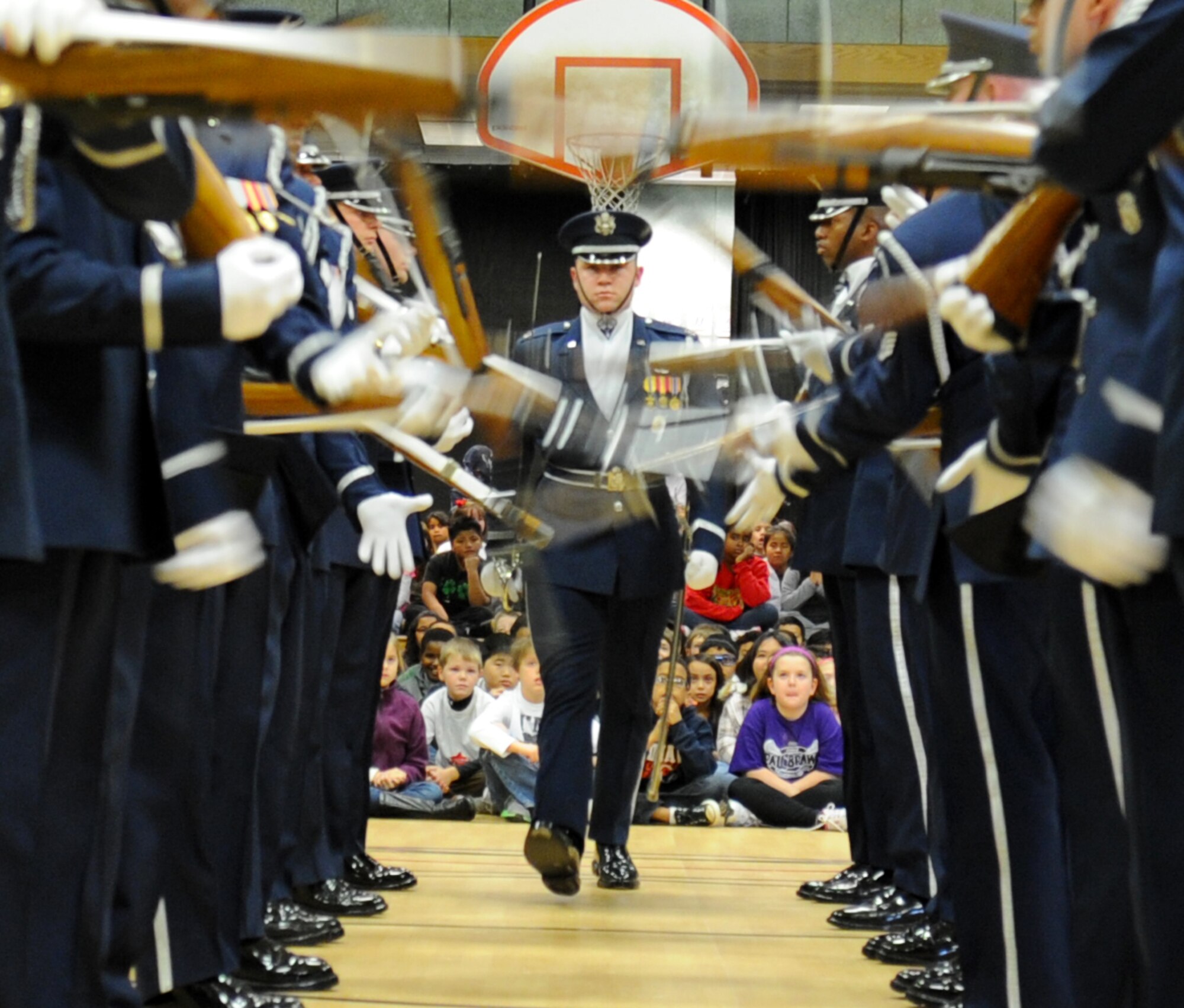 Capt. Alex Stanton, U.S. Air Force Honor Guard Drill Team flight commander, steps confidently forward through a whirlwind of spinning rifles during a performance at Belvedere Elementary School in Falls Church, Va., Nov. 26, 2012.   After the performance, Drill Team members and students planted trees at a plot of land near the school which the students are transforming into Belvedere Park.  (U.S. Air Force photo/Staff Sgt. Torey Griffith)