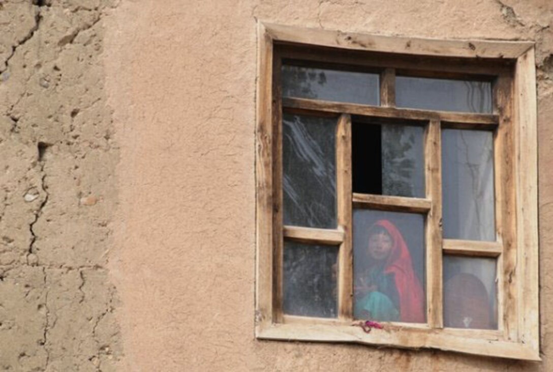 An Afghan girl smiles behind a window in Ghazni province, Afghanistan in 20009. Then-Tech. Sgt. Rebecca Corey was documenting the work of the provincial reconstruction team in the region, when she photographed the child standing in the window observing her team. (U.S. Air Force photo/Master Sgt. Rebecca Corey)