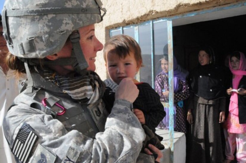 Then-Tech. Sgt. Rebecca Corey smiles as she holds a child while visitng a woman's vocational school in Ghazni province, Afghanistan, during her deployment in 2009. The child was about the same age as Corey's son at the time and the women at the school were surprised that she had a child back at home but was in Afghanistan deployed. (U.S. Air Force photo)
