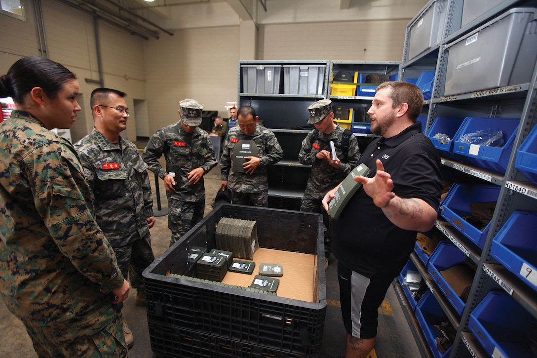 Eddie J. Dunn shows leaders of the Republic of Korea Marine Corps Amphibious Support Group small arms protective inserts during a visit from the ROK Marines to the Individual Issue Facility Nov. 19 at Camp Kinser. The ROK Marines were interested to see the system IIF uses to issue equipment to the Marines of 3rd Marine Logistics Group. Dunn is the site manager for IIF, 3rd MLG, III Marine Expeditionary Force.