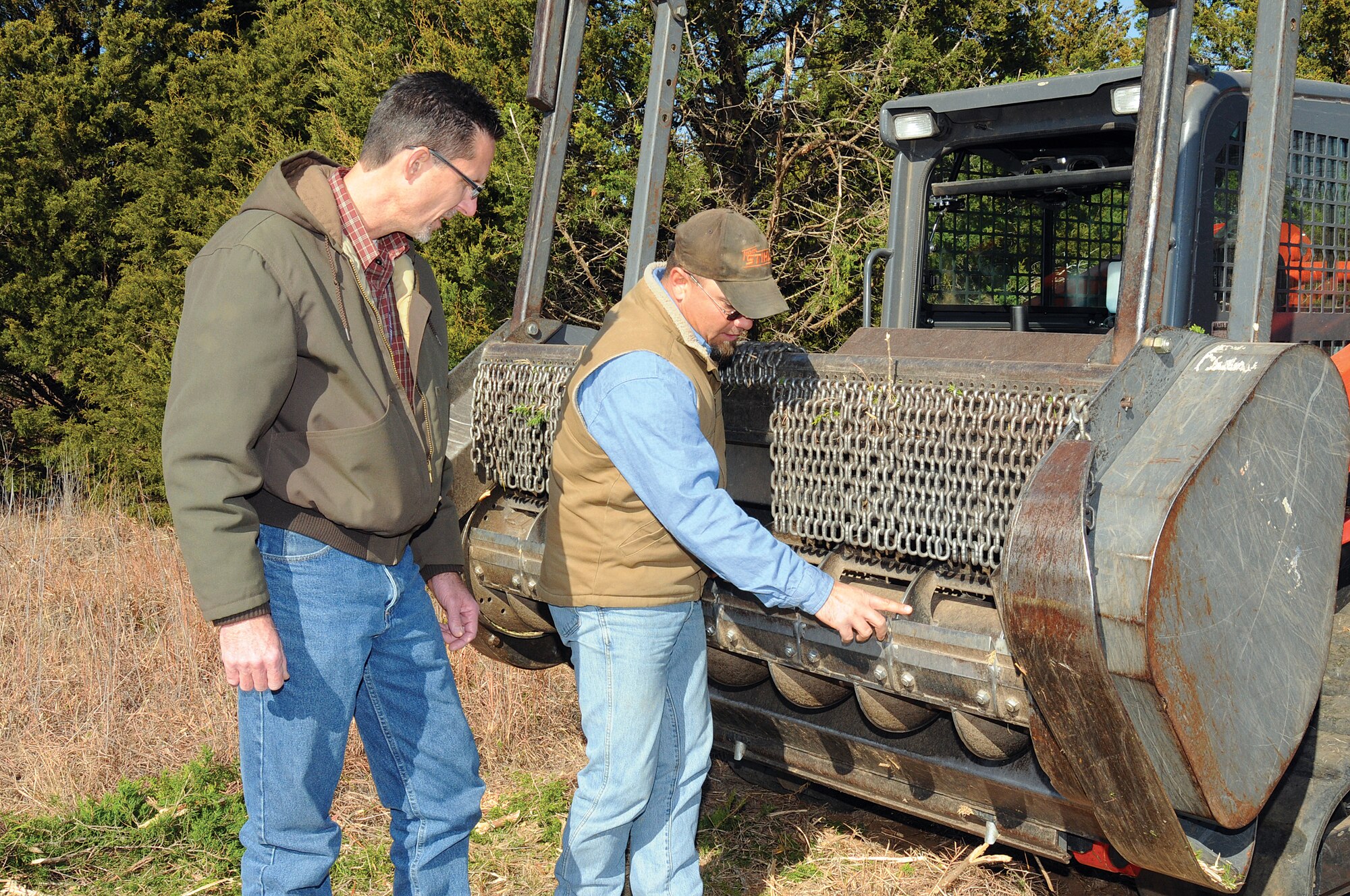 John Krupovage, left, the 72nd Air Base Wing Civil Engineering Directorate natural resources manager, inspects the heavy rotating blade attachment on a skid steer with operator Amando Lujan. Mr. Lujan uses the machine, below, to remove and mulch wild cedars. A 15-foot cedar can be mulched in about two minutes. About 10 acres of cedars have been removed on Tinker this month with another 18 acres to follow. (Air Force photo by Margo Wright)