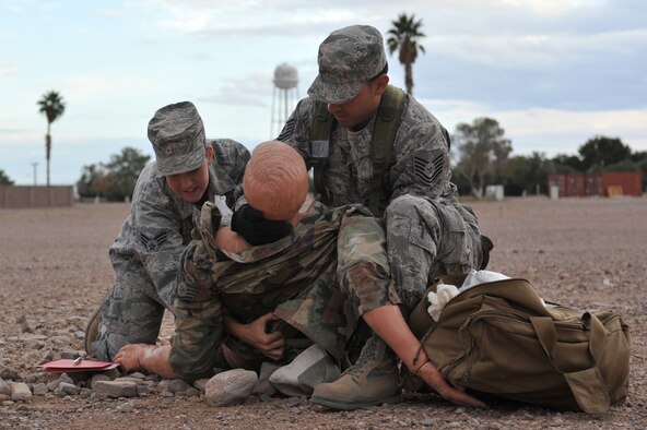 Senior Airman Jennifer King, 56th Civil Engineer Squadron emergency management technician, and Staff Sgt. Adrian Silerio, 56th Civil Engineer Squadron structural craftsman, apply a bandage on a simulated sucking chest wound as part of a self-aid buddy care drill Nov. 8 during bivouac training at Gila Bend Air Force Auxiliary Field, Ariz. (U.S. Air Force photo by Senior Airman Sandra Welch)