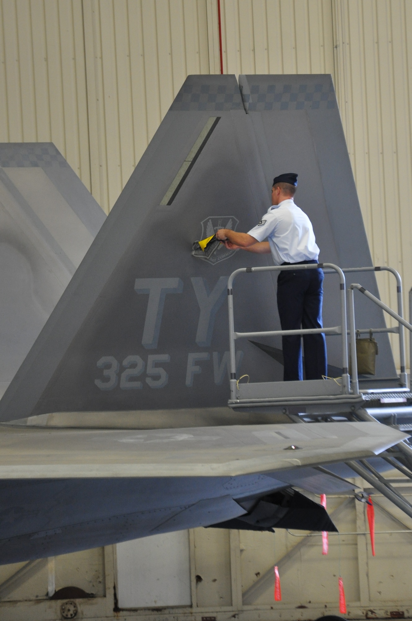 Staff Sgt. Joshua Bard, 325th Aircraft Maintenance Squadron dedicated crew chief, removes the Air Education and Training Command patch from an F-22 Raptor tail, revealing the Air Combat Command patch, Oct. 1 in Hangar 1 during the recent reassignment ceremony. (U.S. Air Force photo by Airman 1st Class Christopher Reel)