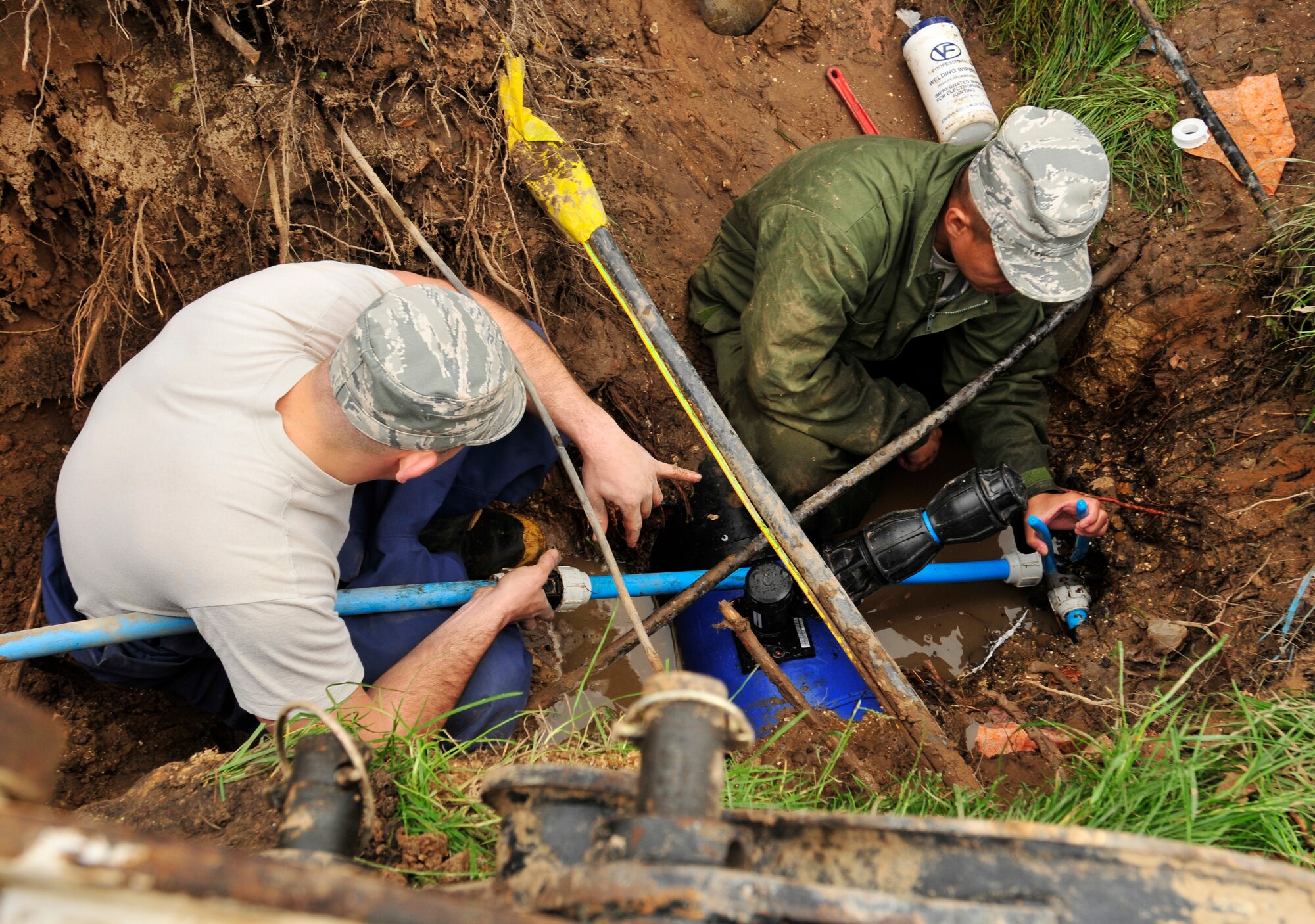 ROYAL AIR FORCE LAKENHEATH, England - Senior Airman Jonathan Wimmer and Staff Sgt. Mervin Brice, 48th Civil Engineer Squadron water and fuels systems maintenance craftsmen, work together to repair a broken waterline outside of building 1063 Sept. 27, 2012. Wimmer holds the pipe steady as Brice cinches it at the opposite end.  This is just one way in which the 48th CES helps shape the installation. (U.S. Air Force photo by Senior Airman Tiffany M. Grigg)