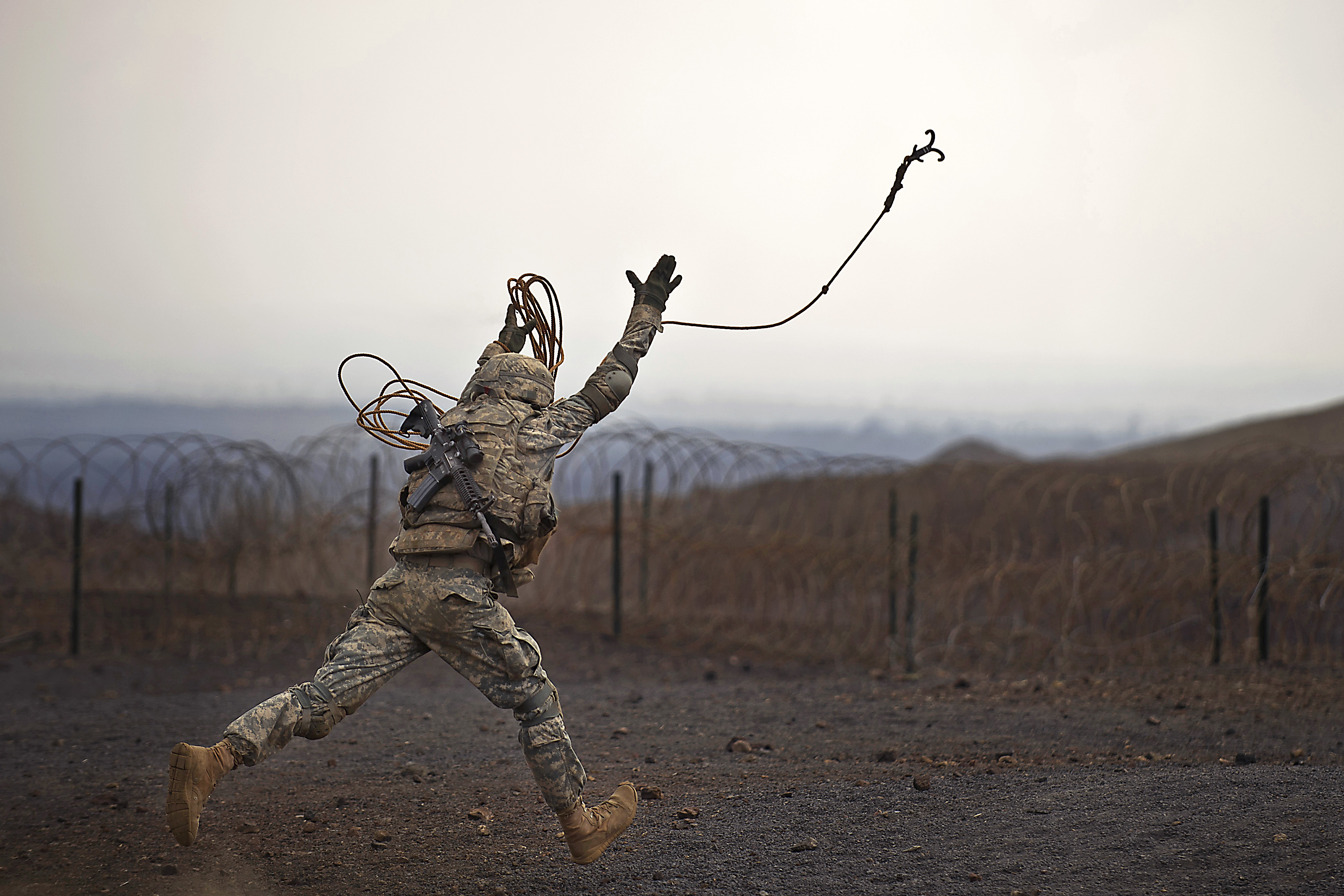 Army Spc. Kyle Norman runs and throws a grappling hook into a simulated  mine field during