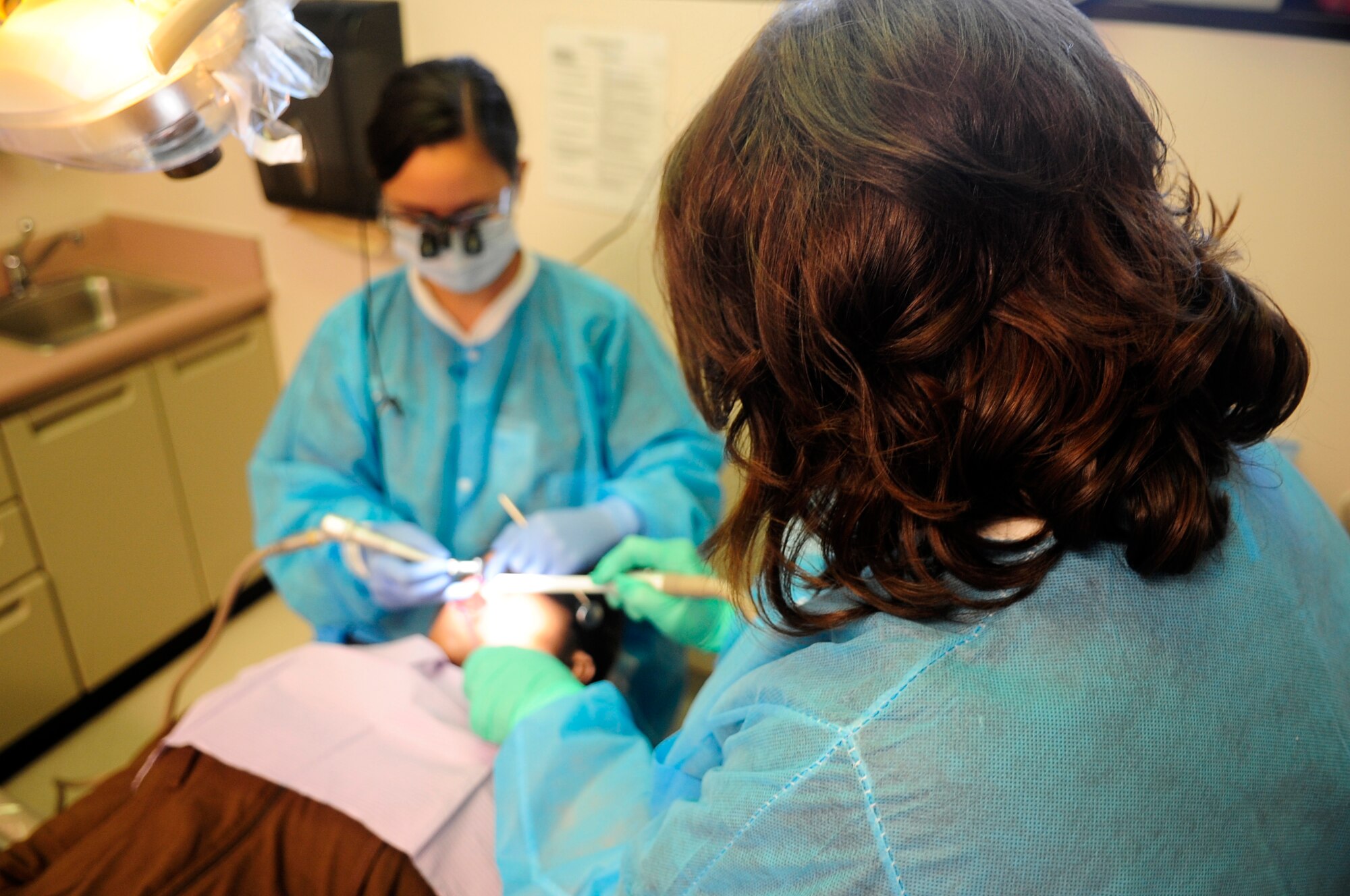 Sunshine Maldanado, dental assistant, helps U.S. Air Force Capt. Jennilyn Estell, 20th Dental Squadron Doctor of Medical Dentistry, with a routine dental examination of patient, Tanya Maisonet, during a training exercise for the Red Cross Volunteer Dental Assistance Program, Shaw Air Force Base, S.C., Sept. 24, 2012. The Red Cross Dental Assistance Program offers dental education to military dependents and spouses, with over 900 hours of both classroom and hands-on training. (U.S. Air Force photo by Airman Hunter Brady/Released) 
